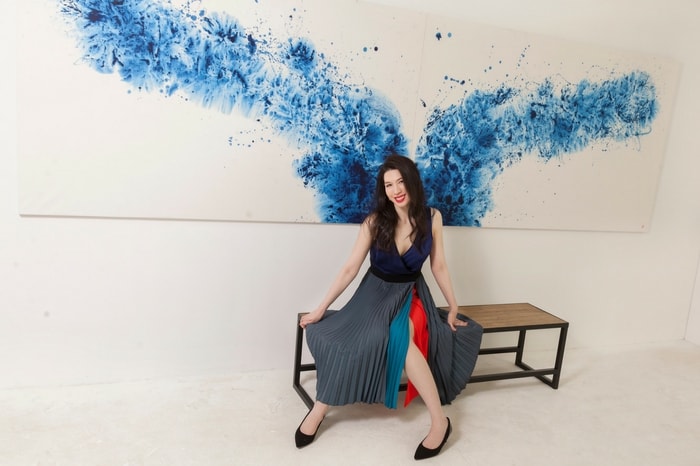 Chloe Ho sits in front of Wellspring, her ink-and-acrylic-on-rice paper creation